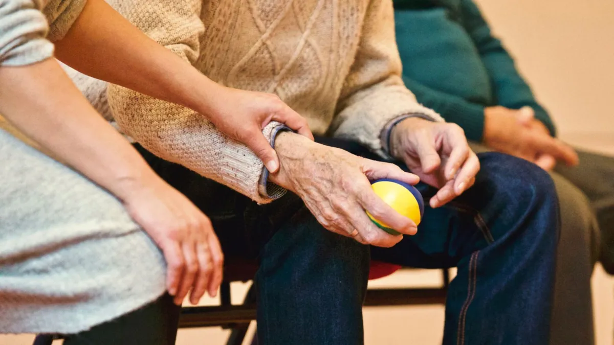 A caregiver supporting an older adult’s hand during therapy